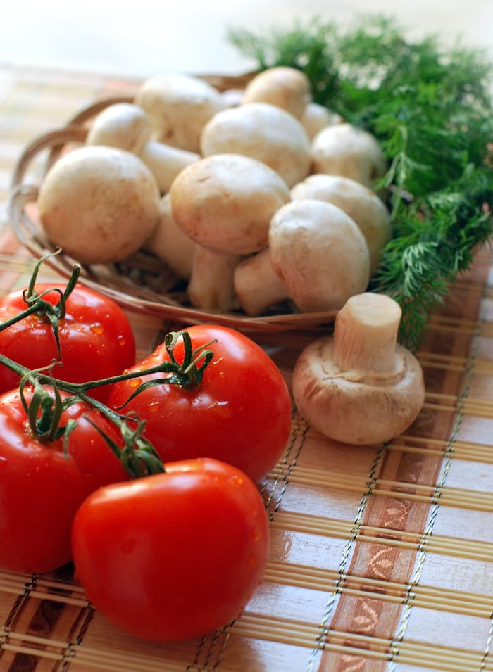 Close-up of fresh tomatoes and mushrooms on a rustic wooden mat, ideal for healthy cooking.